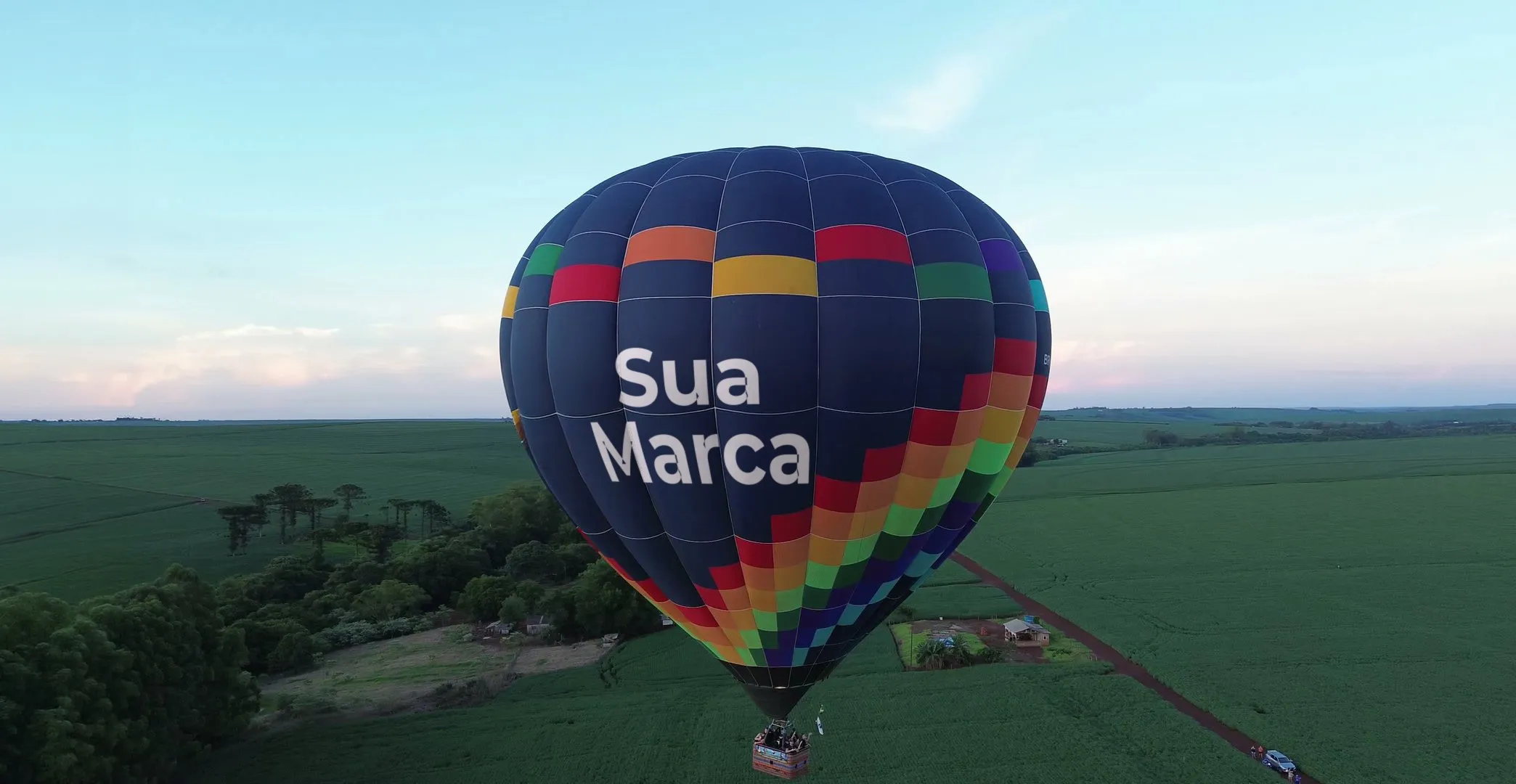 Balão com o espaço 'Sua marca' estampado, voando sobre a mata e as lavouras